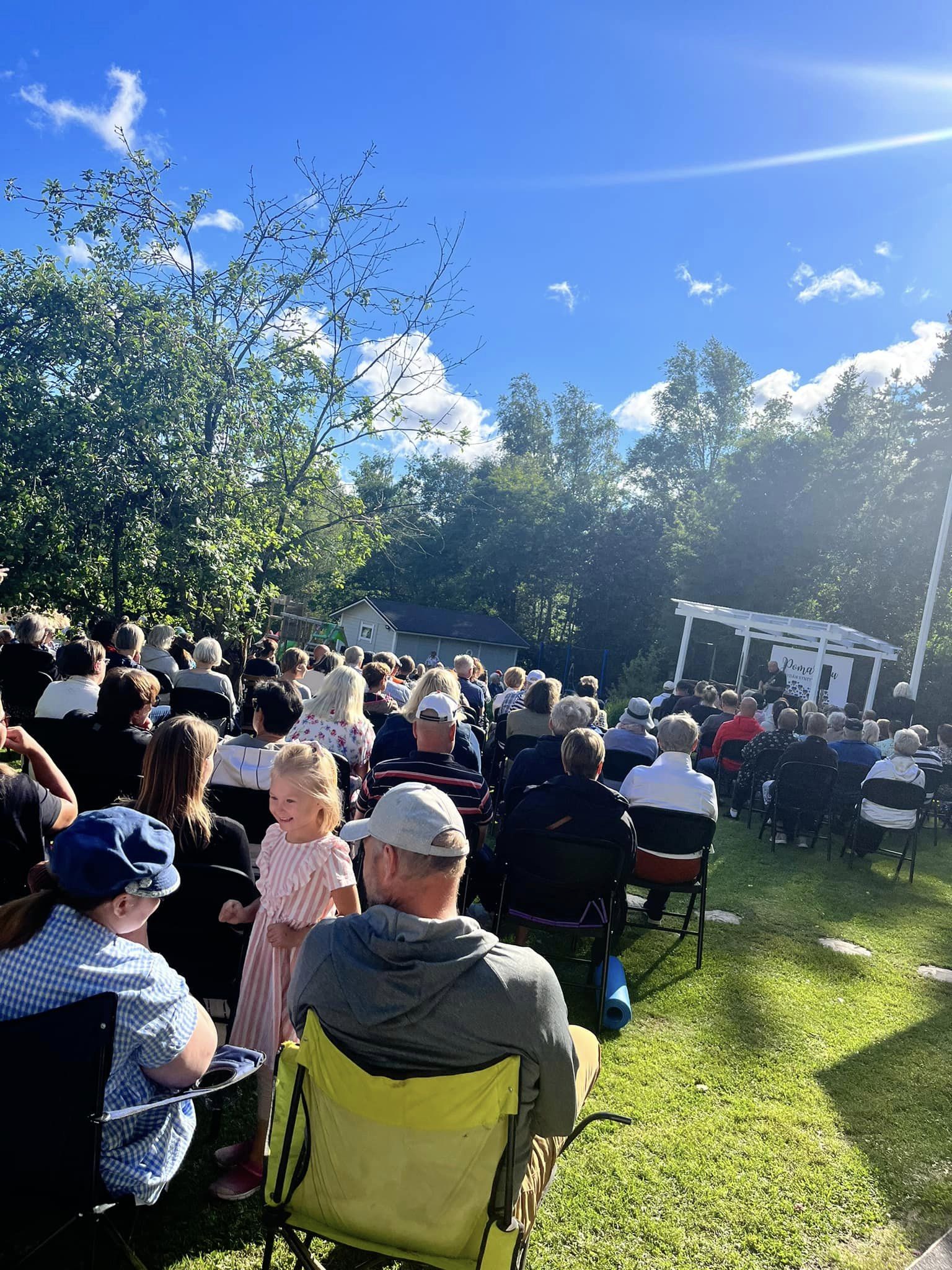 Suuri joukko ihmisiä istuu ulkona tuoleissa.