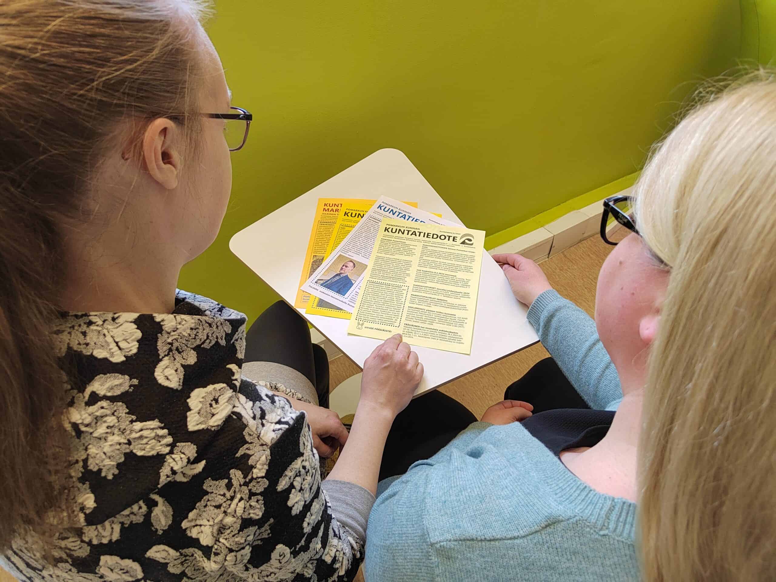 naiset katsovat paperisia kuntatiedotteita