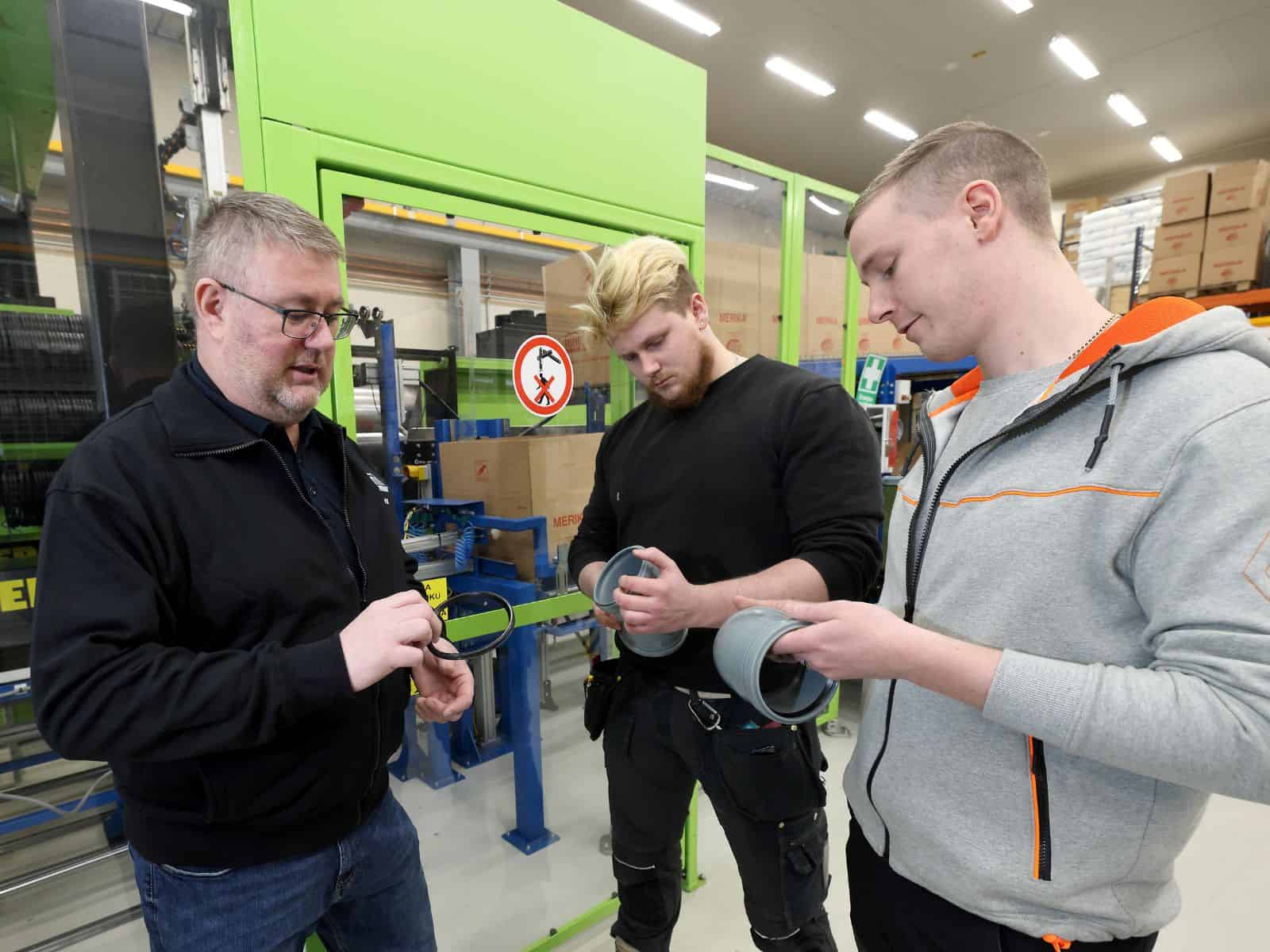 Kolme henkilö seisoo kuvassa vierekkäin teollisuushallin sisällä.