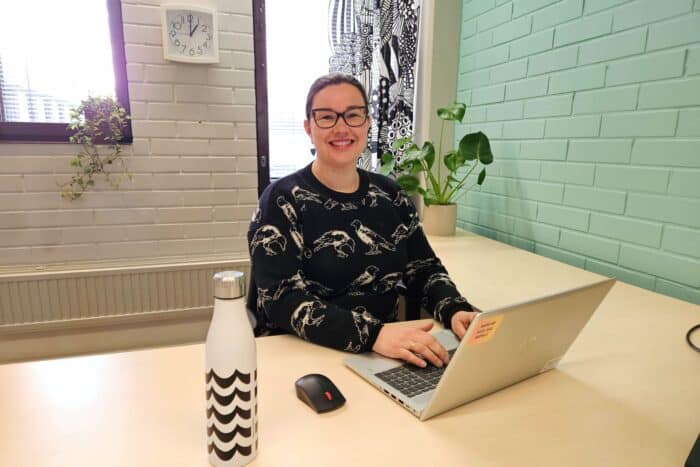 "Henkilö, huone, työpöytä, viherkasvi, juomapullo, seinäkello:"
